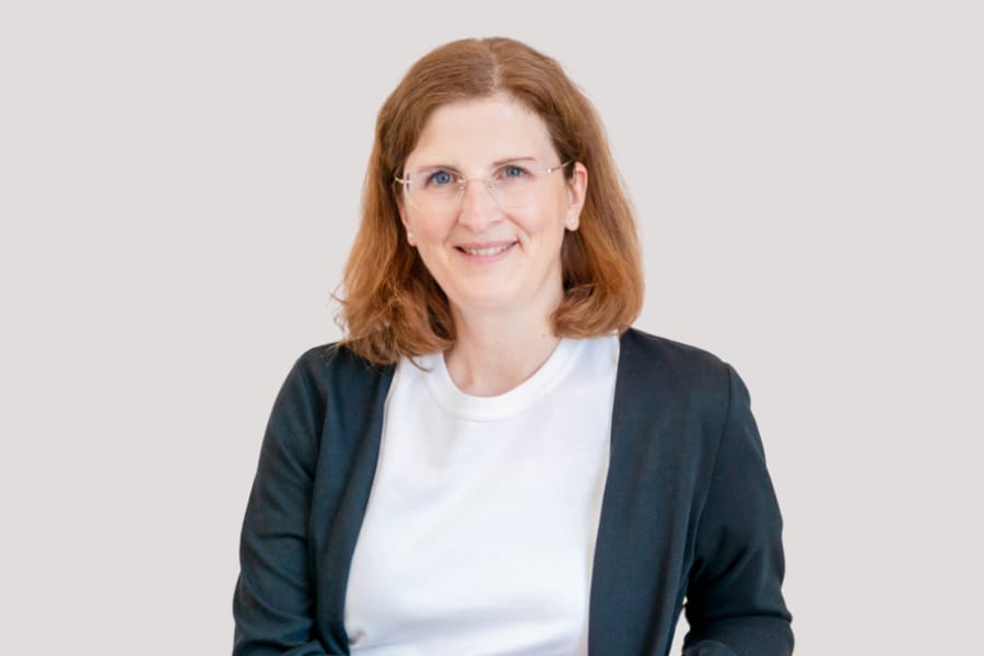 Frau mit Brille und braunen Haaren lächelt.