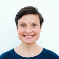 Person mit kurzen Haaren lächelnd vor weissem Hintergrund.