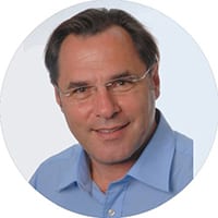 Porträt eines lächelnden Mannes mit Brille und blauem Hemd.