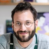 Mann mit Brille und grauem Hemd lächelt.