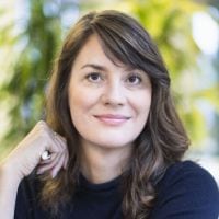 Frau mit braunen Haaren vor unscharfem Hintergrund.