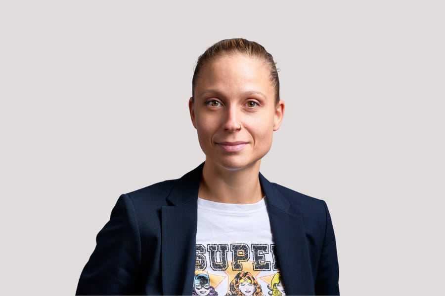 Person in einem dunklen Blazer und T-Shirt vor hellem Hintergrund.