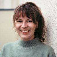 Frau mit grünem Pullover lächelt vor einer Wand.