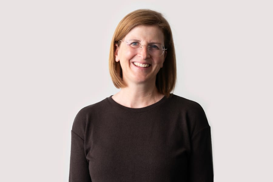Lächelnde Person mit Brille und dunklem Oberteil.