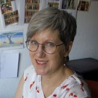 Person mit Brille in einem Raum mit Fotos an der Wand.