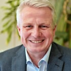 Mann lächelt vor einer Pflanze im Hintergrund.