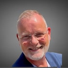 Mann mit Brille lächelt vor grauem Hintergrund.