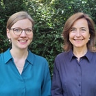 Zwei Frauen lächelnd vor Bäumen im Freien.