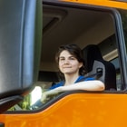 Junge Frau, die aus dem Fenster eines orangefarbenen Lkw lächelt.