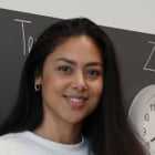 Frau lächelt vor einer Tafel mit Uhr und Schriftzug.