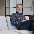 Mann sitzt auf Sofa im Büro mit Kleidung im Hintergrund.