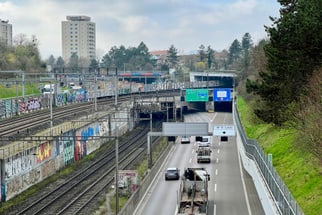 Blick auf Autobahn mit Autos neben Bahngleisen, Gebäude im Hintergrund.