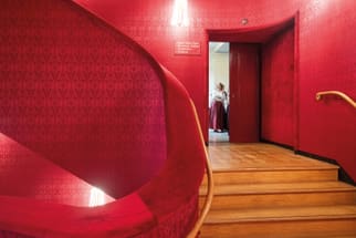Treppe mit rotem Samt, Person im Türrahmen.