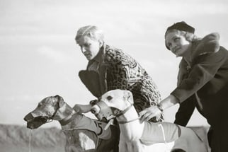 Zwei Frauen halten Rennhunde fest.