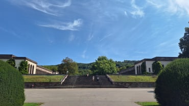 Breite Treppe zwischen symmetrischen Gebäuden und Bäumen unter blauem Himmel.