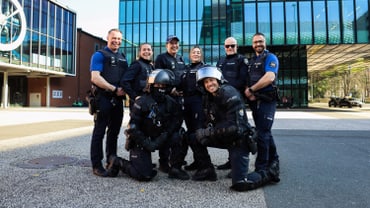 Gruppe von Polizisten posiert vor modernem Gebäude.