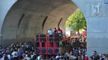 Menschenmenge unter Brücke mit Lautsprechern und DJs.