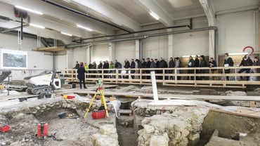 Besucher bei einer archäologischen Ausgrabungsstätte in einer Halle.",