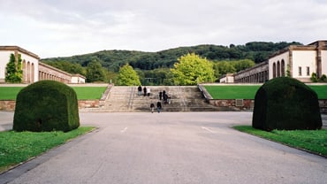 Breite Treppe mit grünen Büschen und Gebäuden im Hintergrund.
