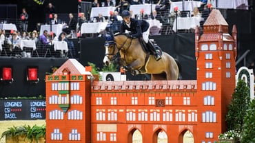 Reiter springt mit Pferd über Hindernis bei einem Turnier in der Halle.",