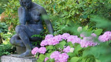 Statue einer sitzenden Frau im Garten mit rosa Blumen.