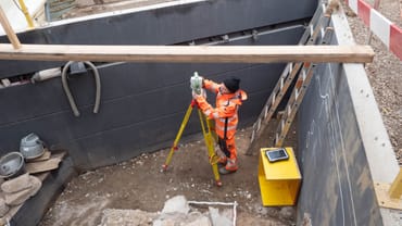 Archäologin mit Vermessungsgerät in Grube auf Ausgrabung.