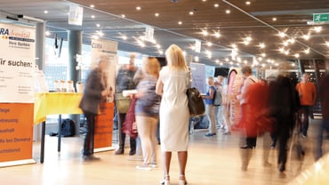 Menschen in beleuchteter Halle mit Werbebannern.