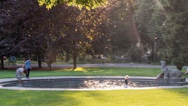 Kinder spielen an einem kleinen Brunnen in einem Park bei Sonnenuntergang.
