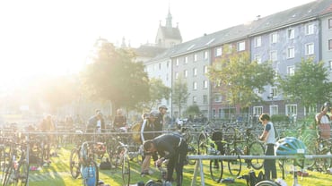 Menschen arrangieren Fahrräder auf einer Wiese bei Sonnenschein.