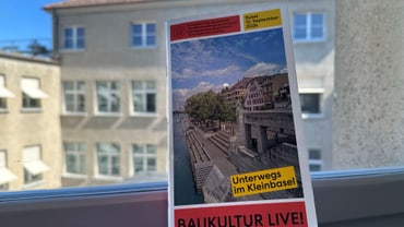 Blick auf ein Gebäude hinter einem Fenster mit einem Plakat im Vordergrund.