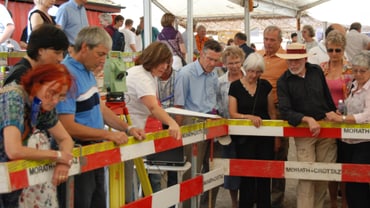 Gruppierung von Menschen hinter einer rot-weiss gestreiften Absperrung.