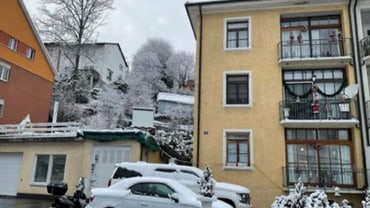 Wohngegend im Winter mit Schnee auf Autos und Gebäuden.
