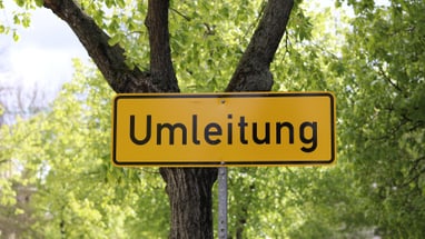 Gelbes Umleitungsschild vor einem Baum.
