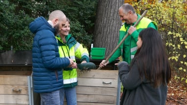 Menschen im Gespräch beim Kompostieren im Freien.",