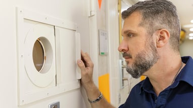 Mann blickt durch ein kreisförmiges Fenster in einer Tür.