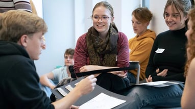Gruppe junger Menschen bei einer Diskussion mit Papier in der Hand.