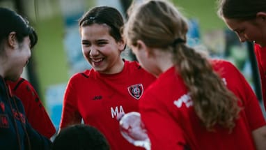 Lachende Mädchen in roten Trikots beim Fussballspiel.