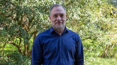 Mann in blauem Hemd vor grünem Hintergrund im Freien.