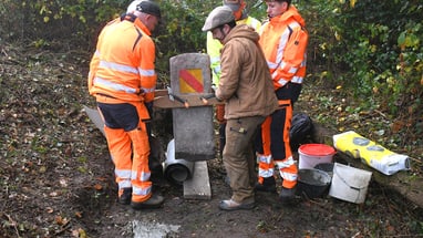 Arbeiter in orangefarbener Kleidung richten einen Grenzstein aus.