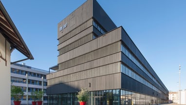 Modernes, eckiges Gebäude mit Holzfassade bei klarem Himmel.