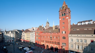 Blick auf den roten Rathausturm und den Marktplatz in Basel bei klarem Himmel.