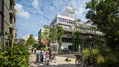 Moderne Wohnsiedlung mit Fahrradfahrern und Bäumen.