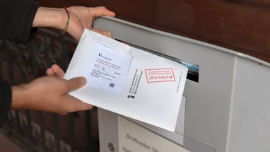 Hand, die einen Brief in einen Briefkasten wirft.