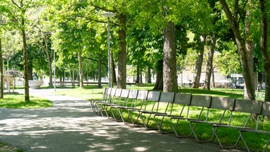 Parkweg mit Bänken und Bäumen an einem sonnigen Tag.