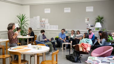 Das Kollegium vom Isaak Iselin in einem Gemeinschaftsraum sitzend und diskutierend.