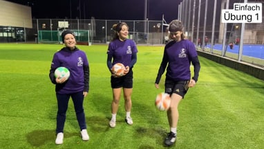 Drei Frauen mit Bällen auf einem Fussballplatz bei Nacht.