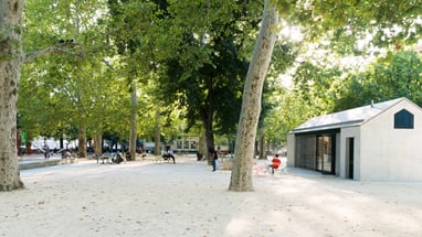 Park mit Bäumen, kleinem Gebäude und Personen im Freien.