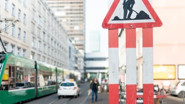 Baustellenschild auf einer Stadtstrasse mit Strassenbahn und Autos.