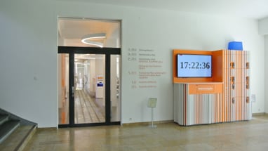 Flur mit digitaler Uhr und Türen im Gebäudeinneren.