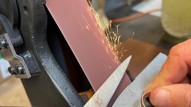 Schere wird an Schleifmaschine geschärft, Funken fliegen.